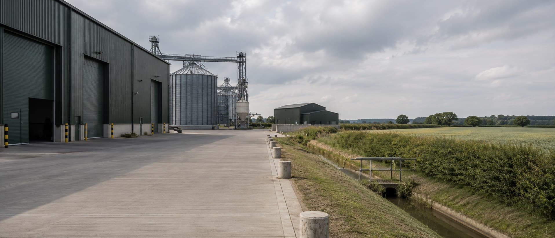 A modern farm building beside a field edge and hedgerow.