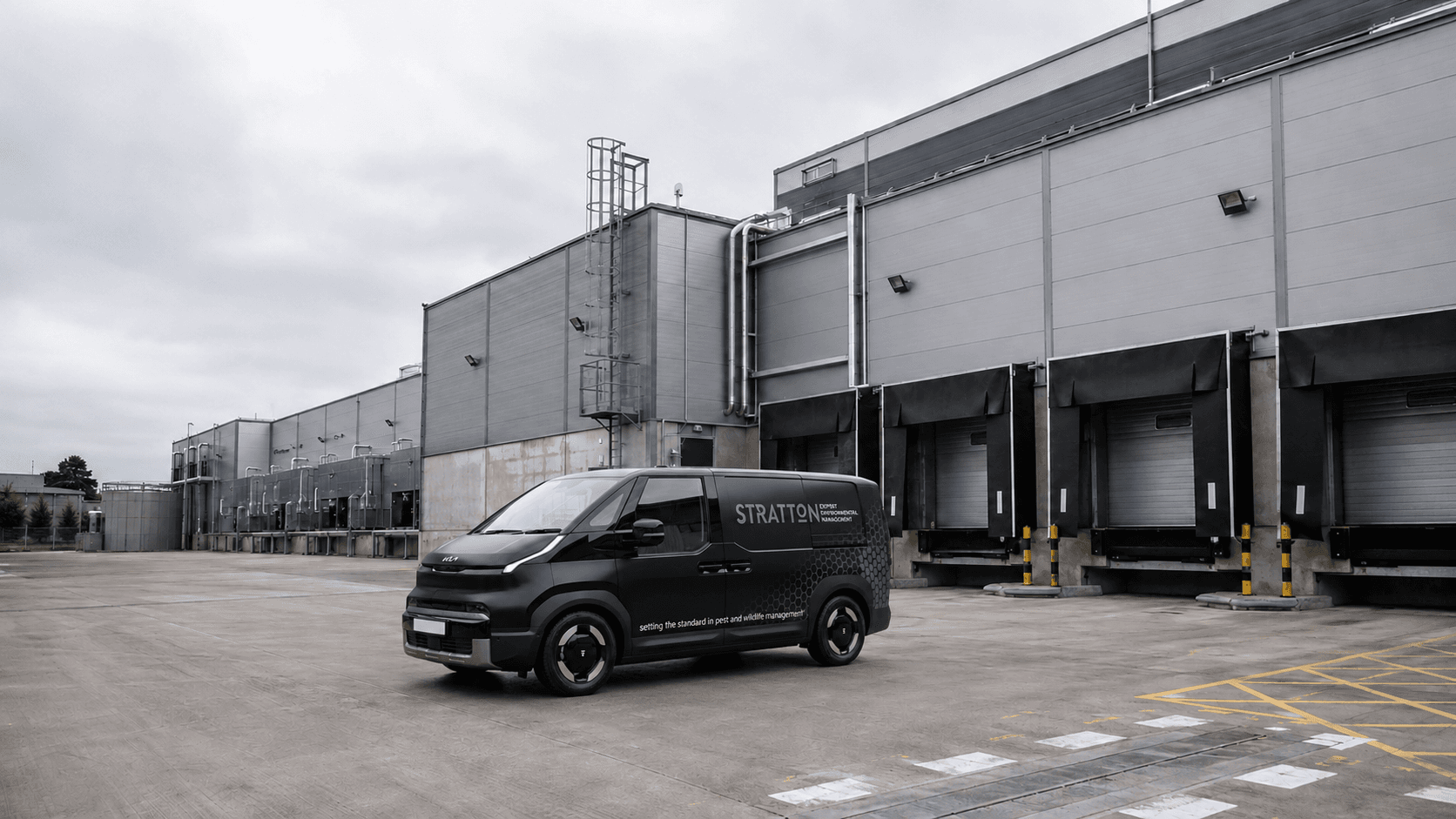 A branded Stratton van on the wet service yard of a commercial distribution site with loading-bay docks.