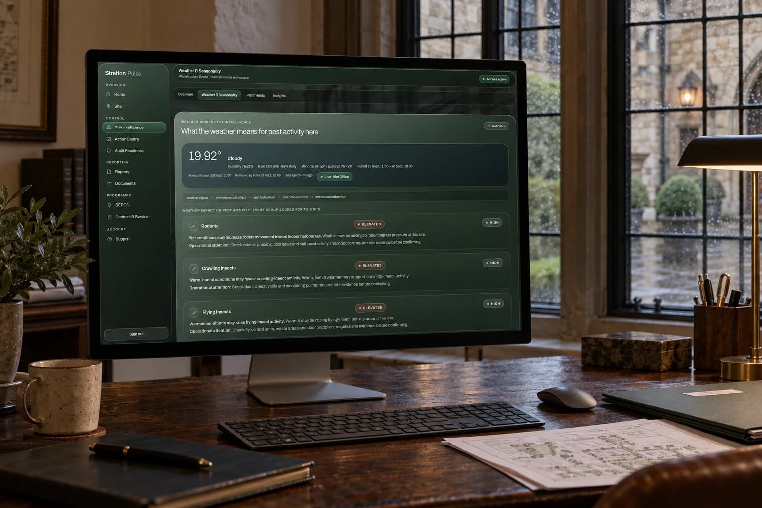 Stratton Pulse on a monitor in a stone-walled office on a wet day: the Weather & Seasonality view, with a live Met Office forecast and the weather’s likely effect on rodents, crawling insects and flying insects at the site.